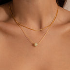 Close-up of model wearing a delicate gold chain necklace featuring a single round green jade bead, layered with a dainty box chain necklace.