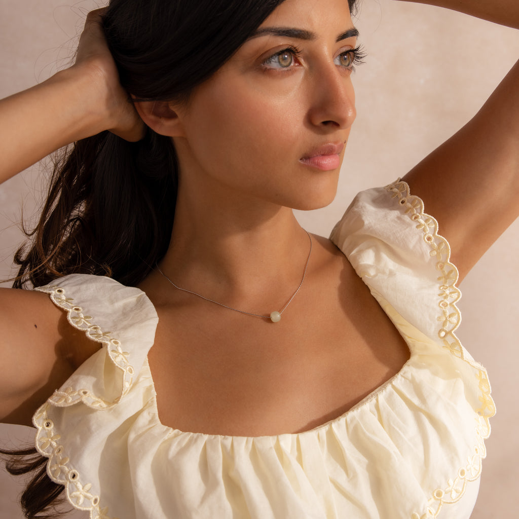 Far-view of a model wearing a delicate silver chain necklace featuring a single round green jade bead, styled with a flowy cream top.