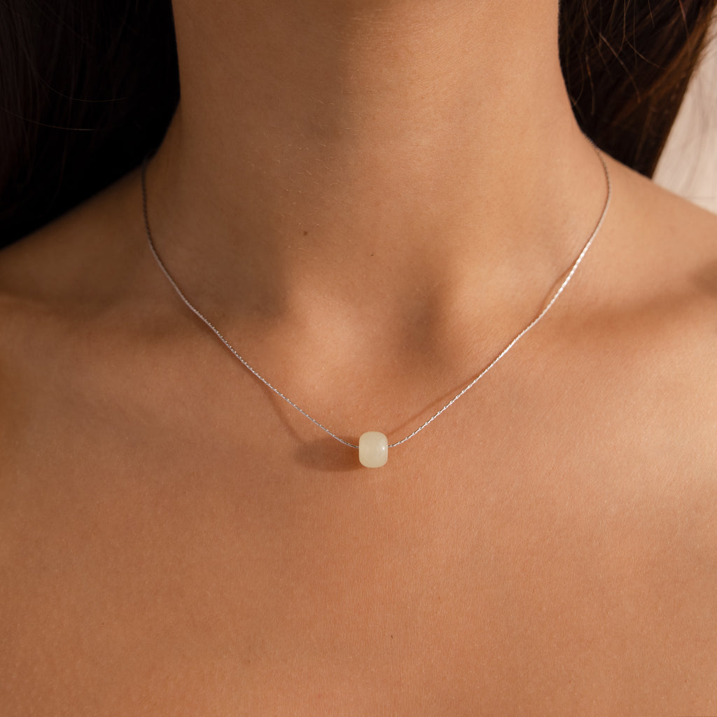 Close-up of a model wearing a delicate silver chain necklace featuring a single round green jade bead.