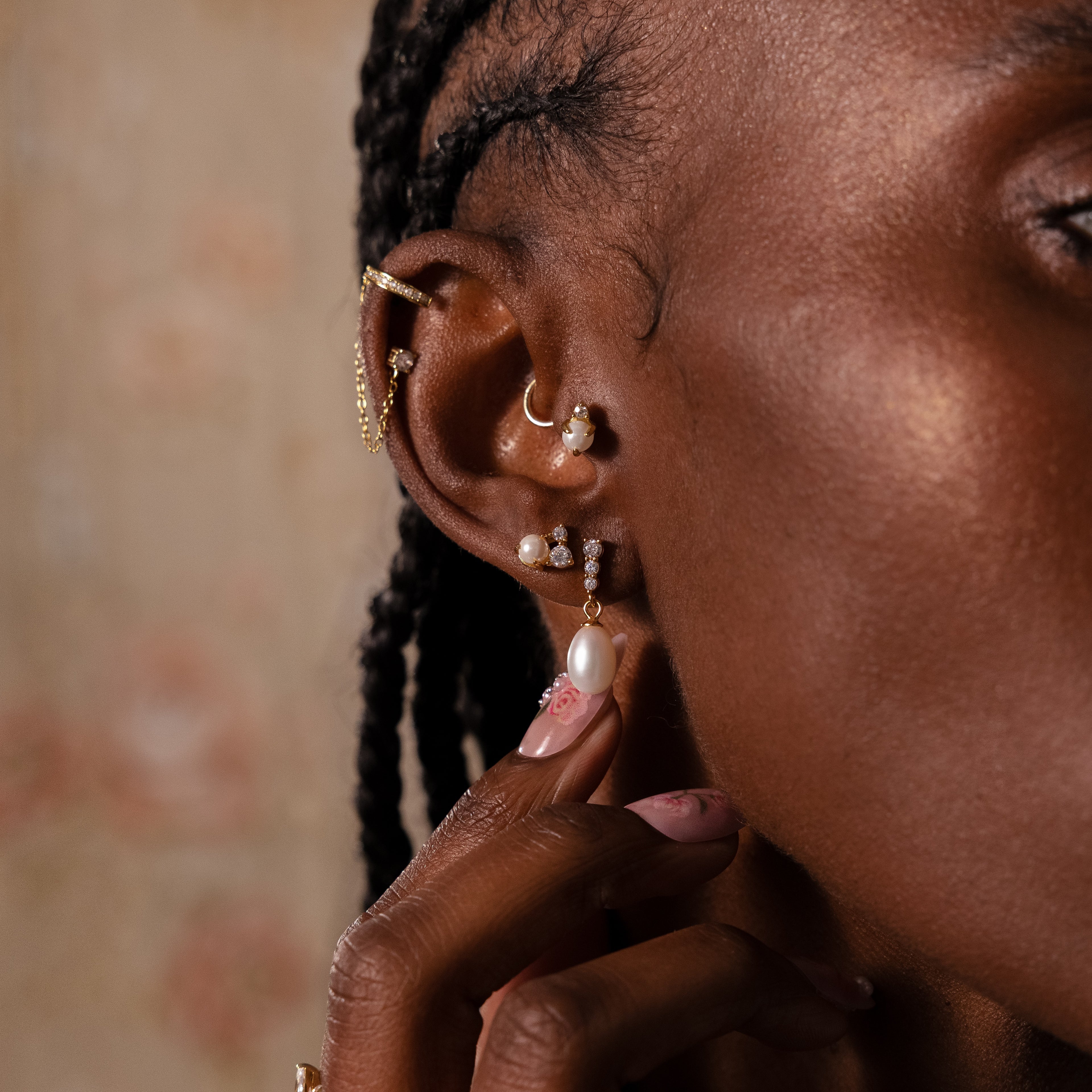 Close-up of an ear with braided hair wearing Pearl Diamond Cluster Studs—gold earrings featuring CZ diamond accents and pearls—with a hand touching a dangling earring.