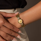 Someone wears the Diamond Mesh Timepiece, featuring a vintage look with a gold mesh band and diamond-accented round face, on their left wrist.