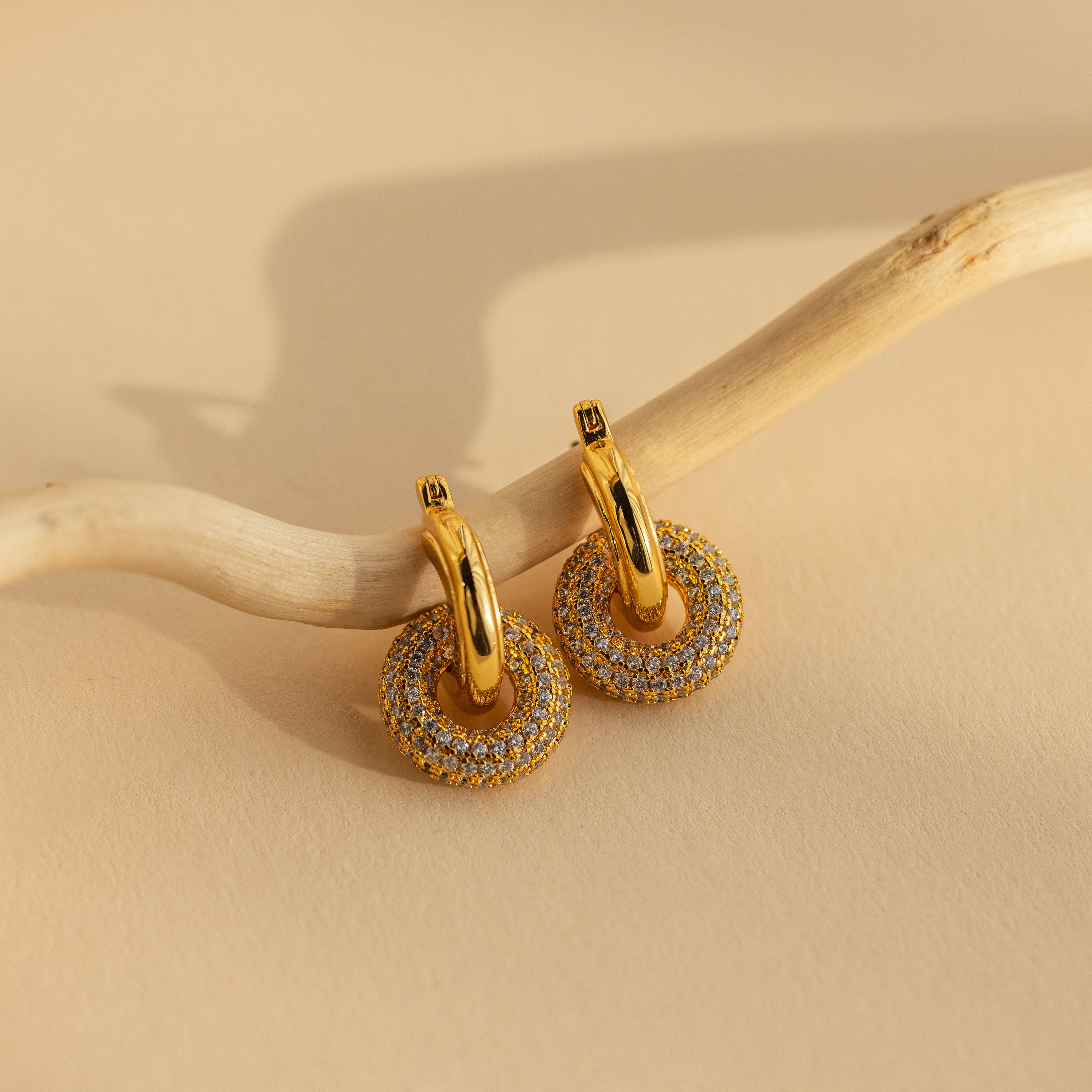 Duo Pave Link Hoops in 18K Gold with circular, CZ diamond-studded pendants displayed on a light wooden branch.