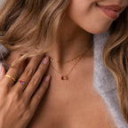 A woman wearing a Multiple Teardrop Birthstone Necklace and a red gemstone ring touches her chest, her wavy hair framing a soft smile—making this personalized necklace a truly meaningful gift.