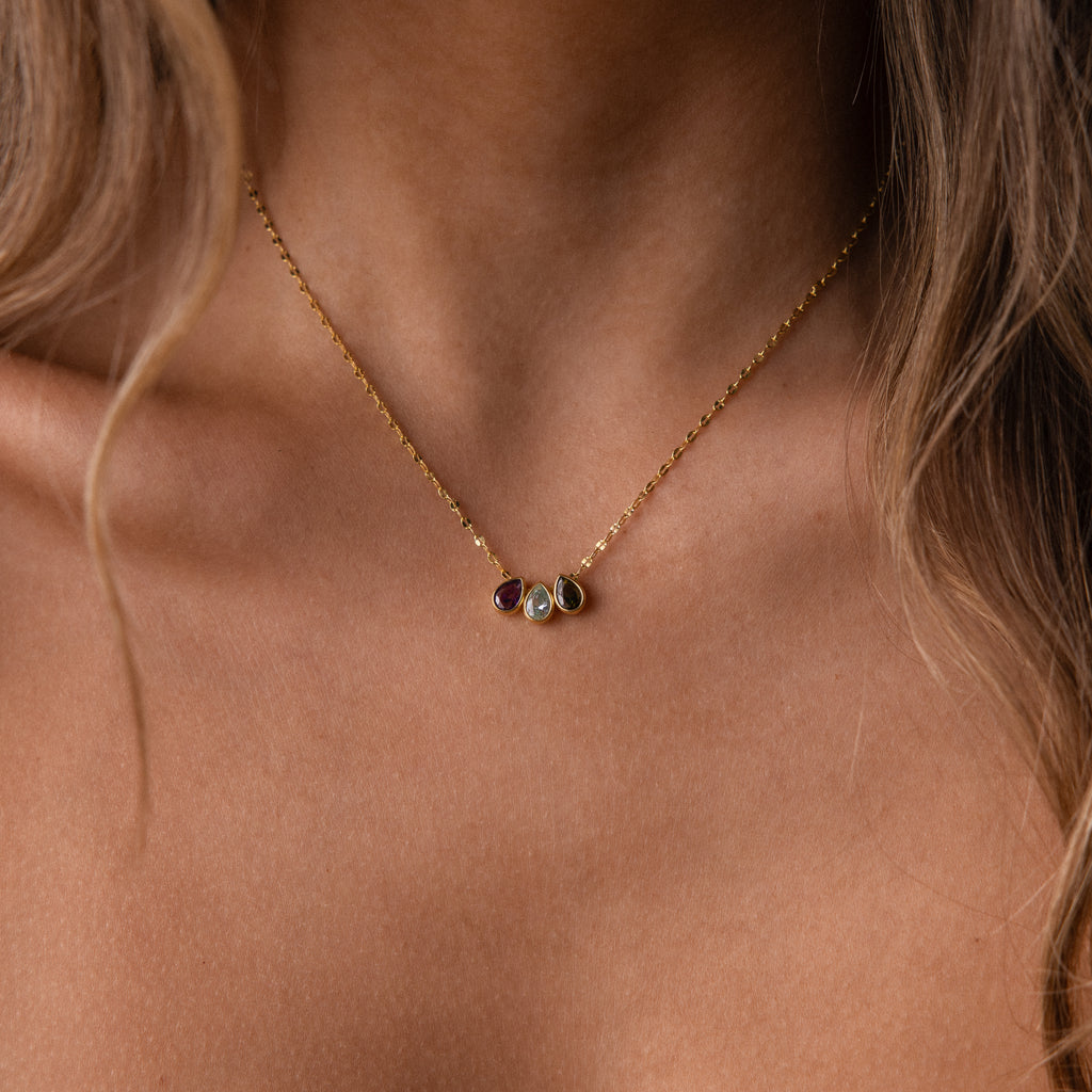 The Multiple Teardrop Birthstone Necklace features three small gemstone pendants on a gold chain, shown close-up at the collarbone—a stunning personalized jewelry piece and meaningful gift.
