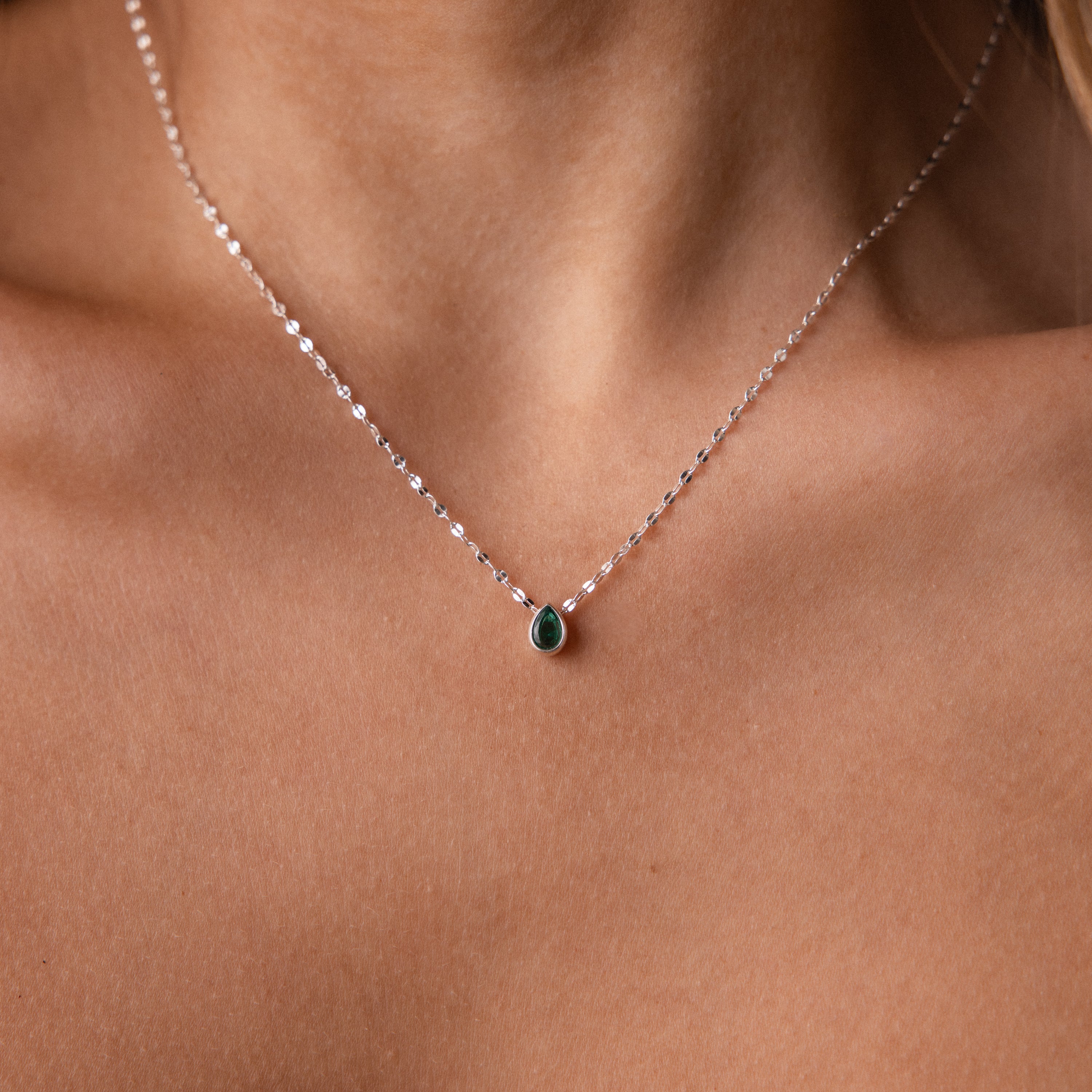 Close-up of a woman’s neck wearing the Multiple Teardrop Birthstone Necklace, featuring delicate silver teardrops and a small green birthstone pendant—an elegant, meaningful gift for someone special.