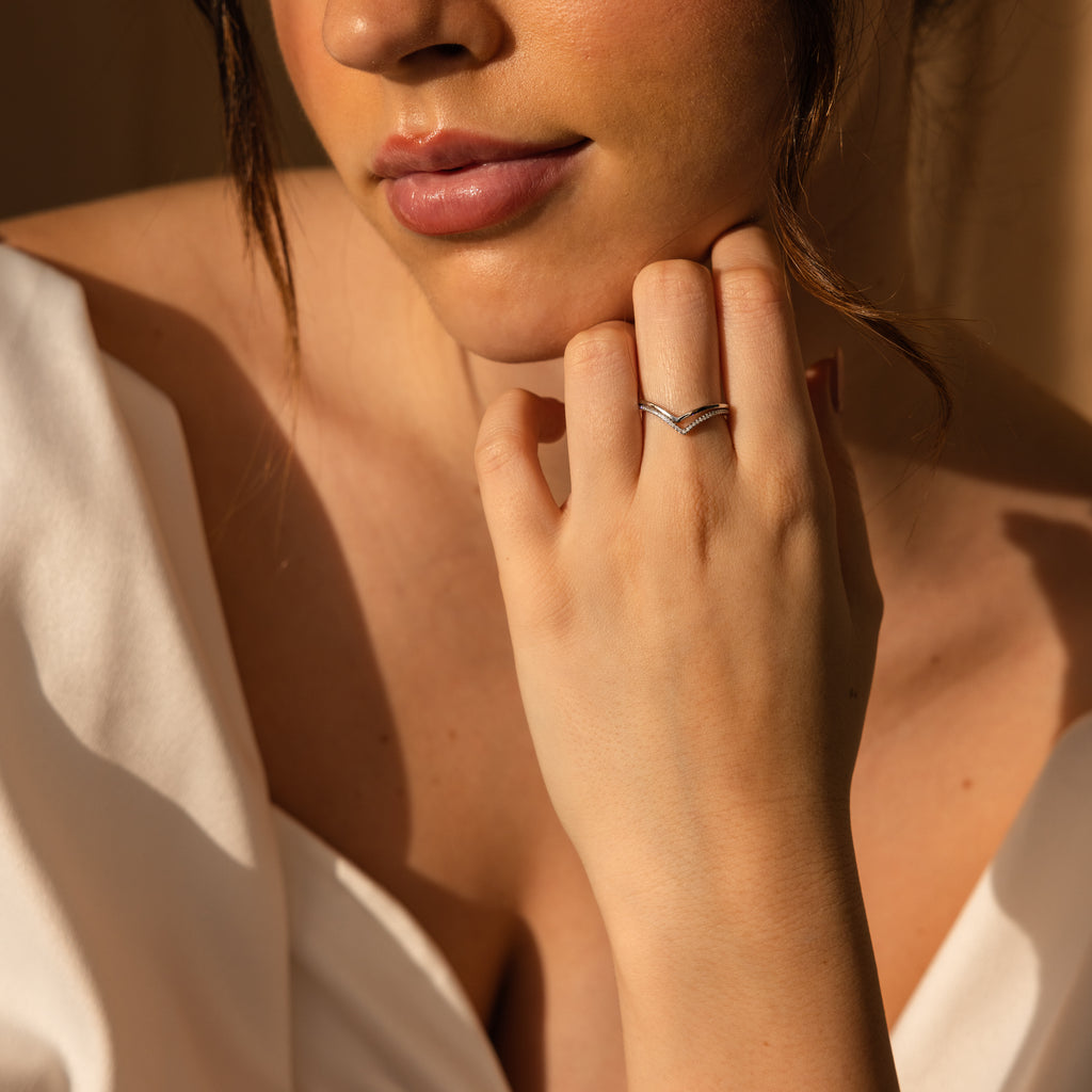 A woman in a white top showcases the Curve Stacking Set in Silver—delicate thin bands on her hand—with soft natural lighting highlighting her face.
