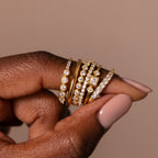 A hand with nude polish displays five Art Deco Diamond Rings, each set in 18K gold and adorned with sparkling clear gemstones, exuding vintage glamour and elegance.