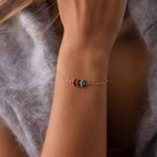 A Multiple Marquise Birthstone Bracelet featuring red, blue, and clear stones adorns a woman's wrist, beautifully matching her soft gray sweater—a stunning customizable birthstone jewelry piece.