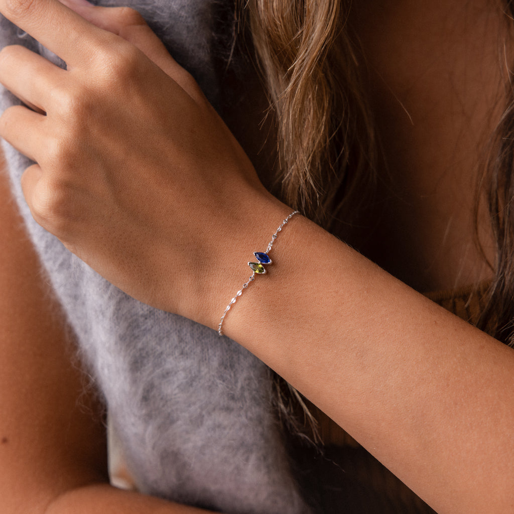 A woman's wrist adorned with the Multiple Marquise Birthstone Bracelet, a delicate silver piece featuring small blue and green gemstone charms.