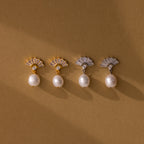 Two pairs of Art Deco Pearl Drop Earrings—one gold, one silver—featuring fan-shaped vintage glamour with pearls, are displayed on a brown background.