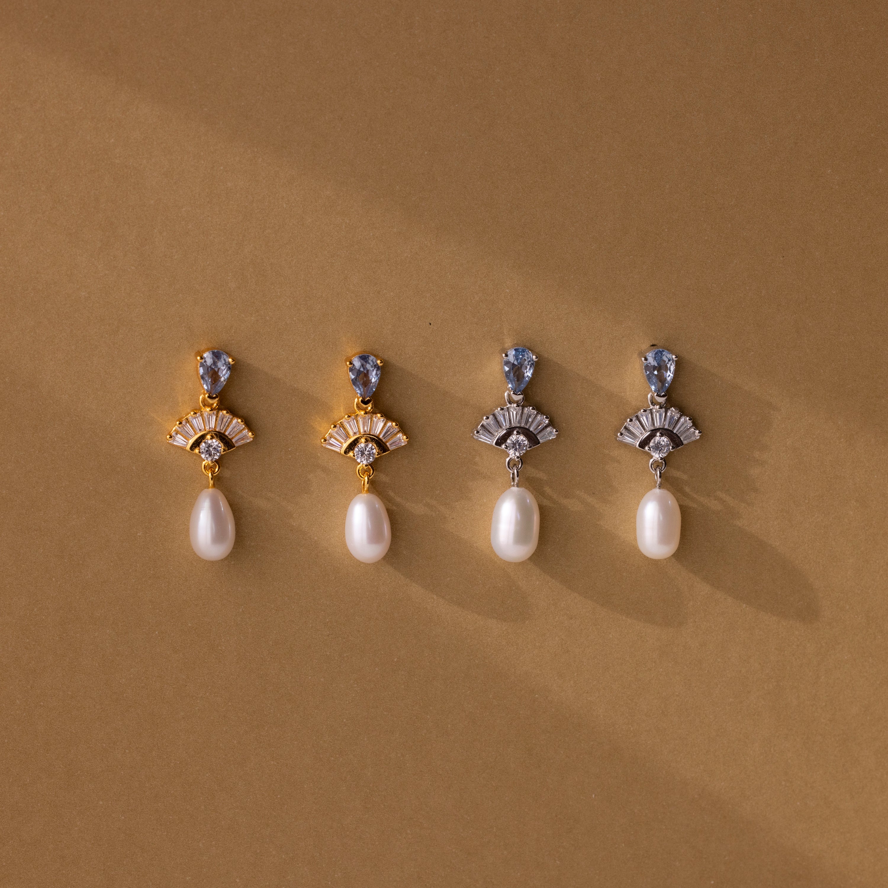 Four pairs of Aquamarine Pearl Drop Earrings—two gold, two silver—capture vintage glamour with pearls on a brown background. Timeless and elegant, perfect as wedding earrings.