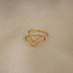 The Curve Stacking Set in 18K Gold—one plain band and one with diamonds—rests on textured cream fabric, perfect for a delicate ring stack.