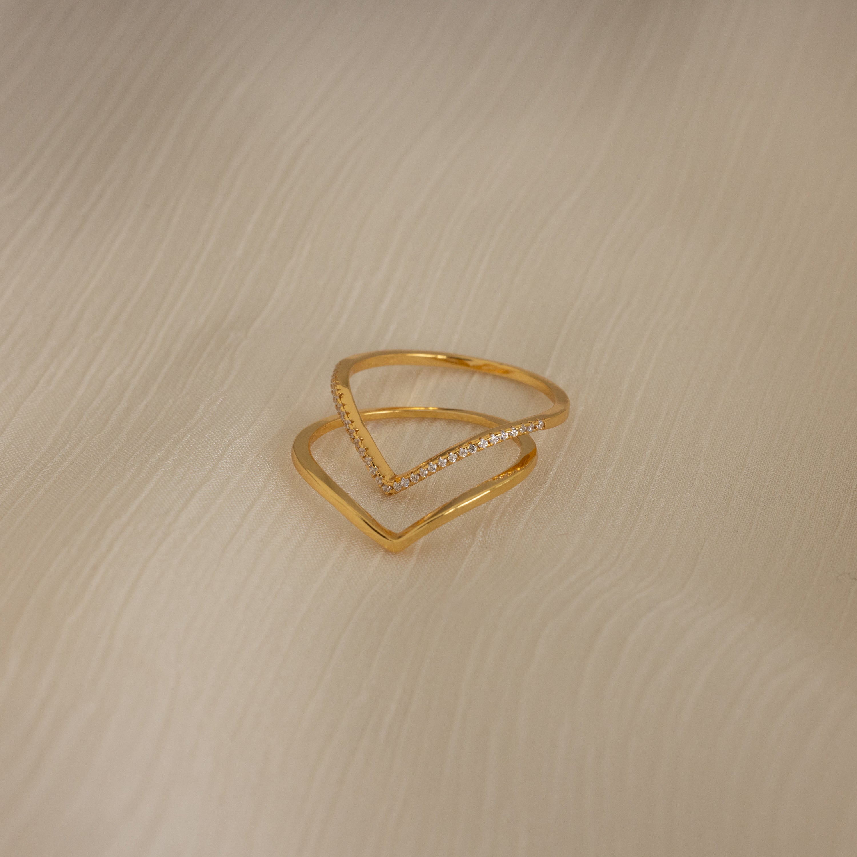 The Curve Stacking Set in 18K Gold—one plain band and one with diamonds—rests on textured cream fabric, perfect for a delicate ring stack.