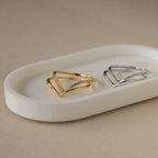 The Curve Stacking Set features two minimalist V-shaped thin band rings, one gold and one silver with small stones, displayed on a white tray.