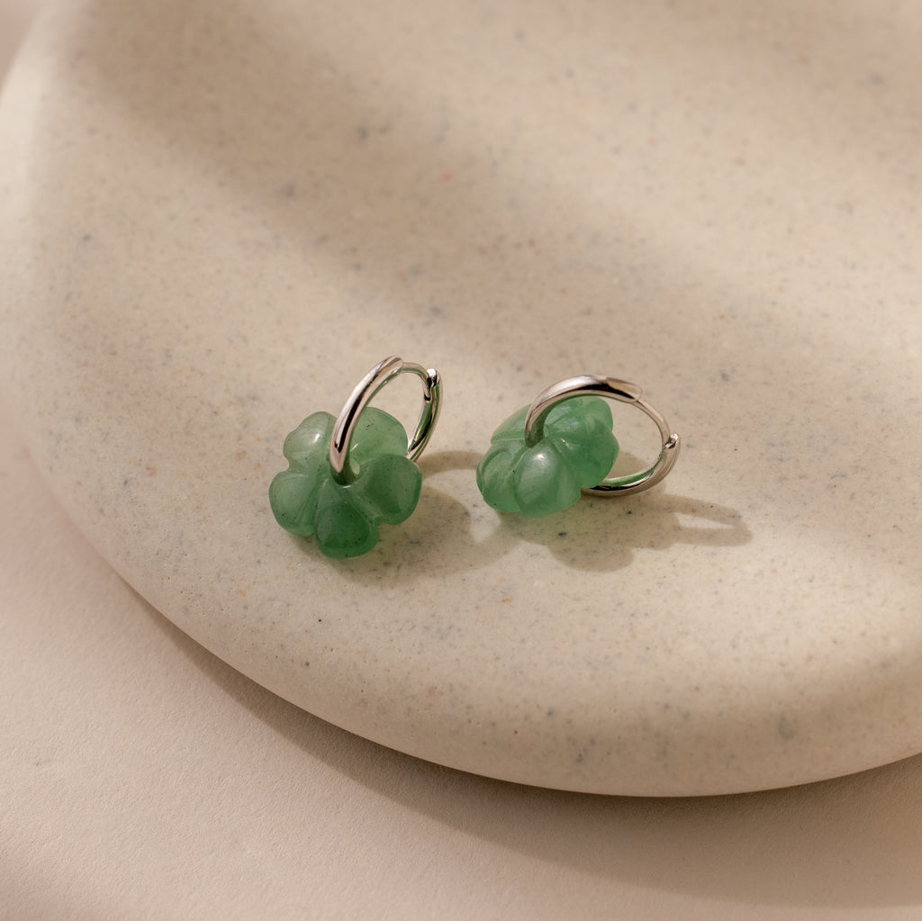 Jade Flower Hoops with green charms rest on a beige ceramic dish—dainty earrings that make a meaningful gift.