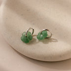 Jade Flower Hoops with green charms rest on a beige ceramic dish—dainty earrings that make a meaningful gift.