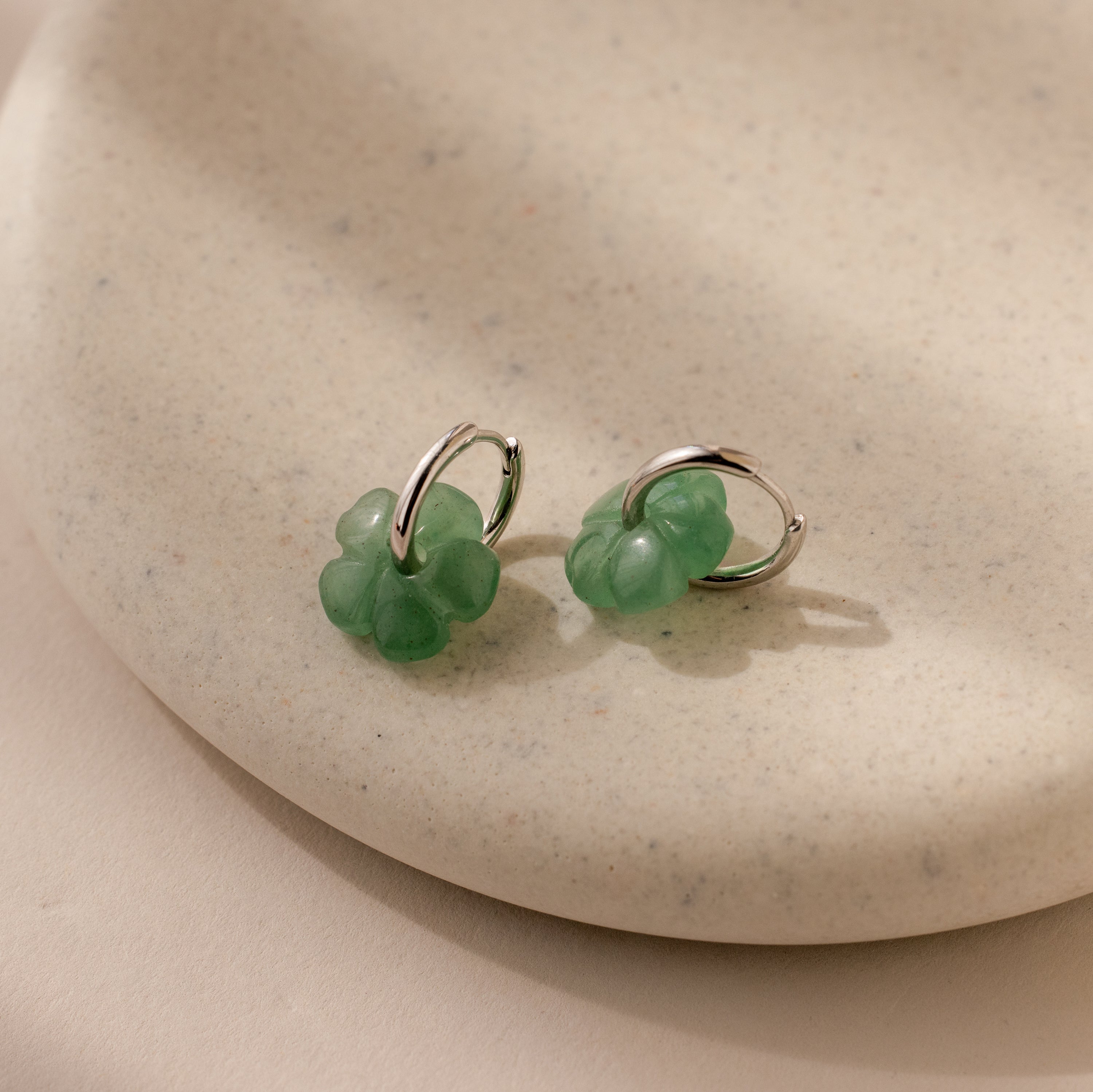 Jade Flower Hoops with green charms rest on a beige ceramic dish—dainty earrings that make a meaningful gift.