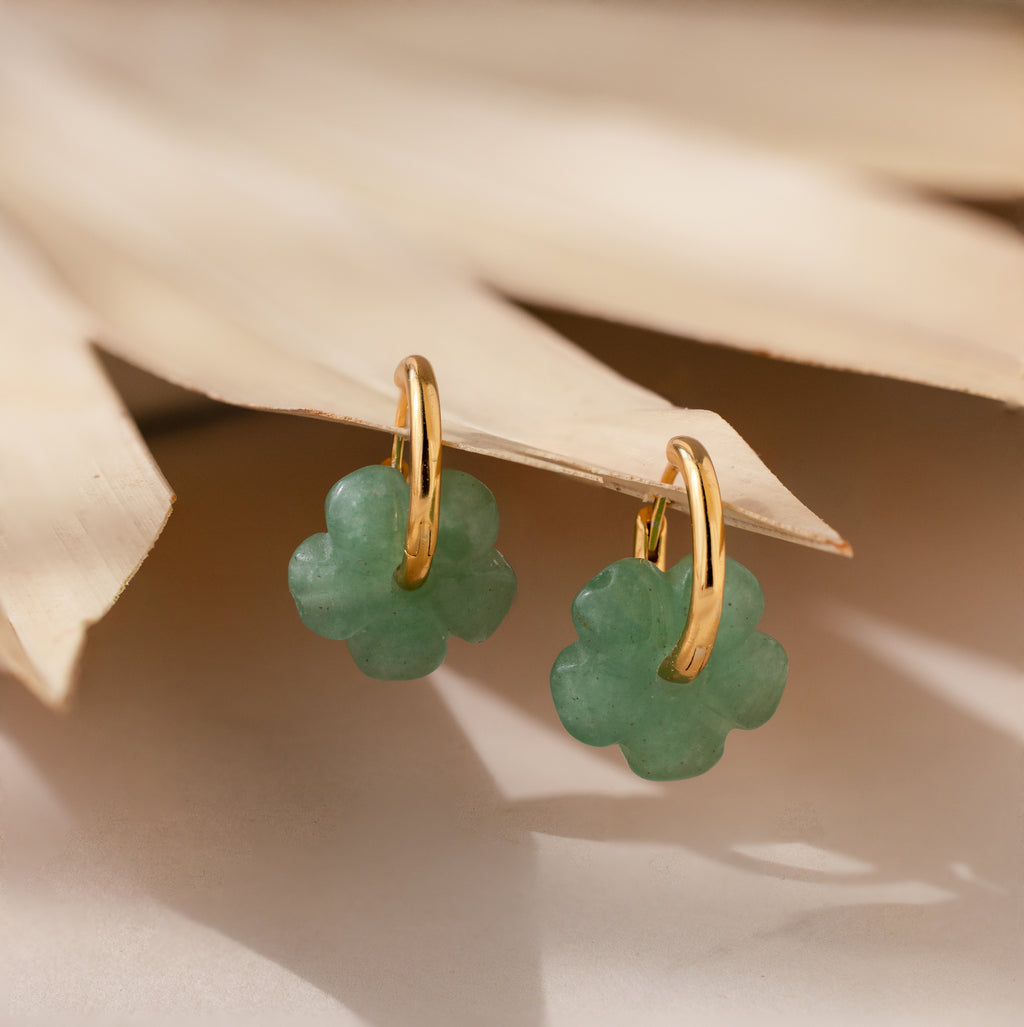 Jade Flower Hoops: Gold hoop earrings with green clover-shaped charms, displayed on a dried palm leaf—these dainty earrings make a meaningful gift.