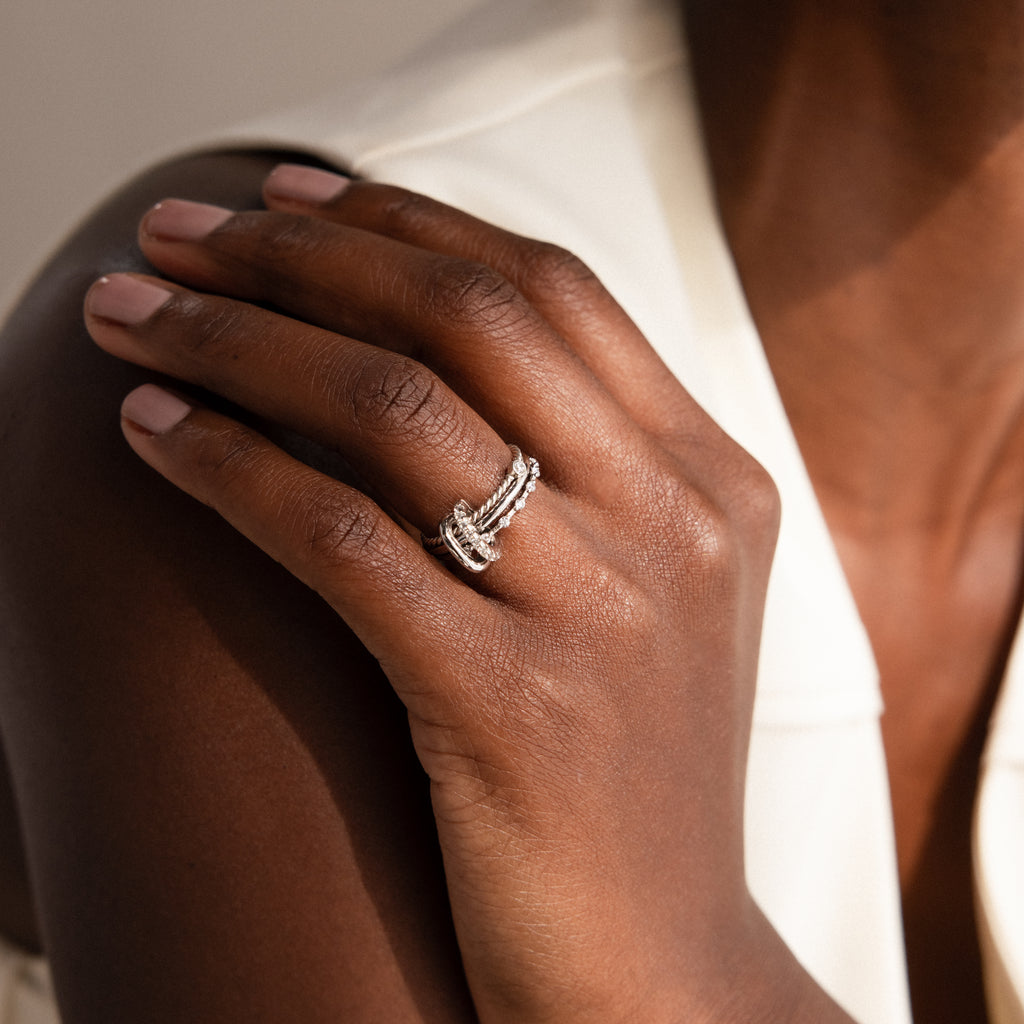 A hand with manicured nails wears stacked silver rings, featuring the Multipurpose Pave Ring Lock Set, against a white sleeveless top.