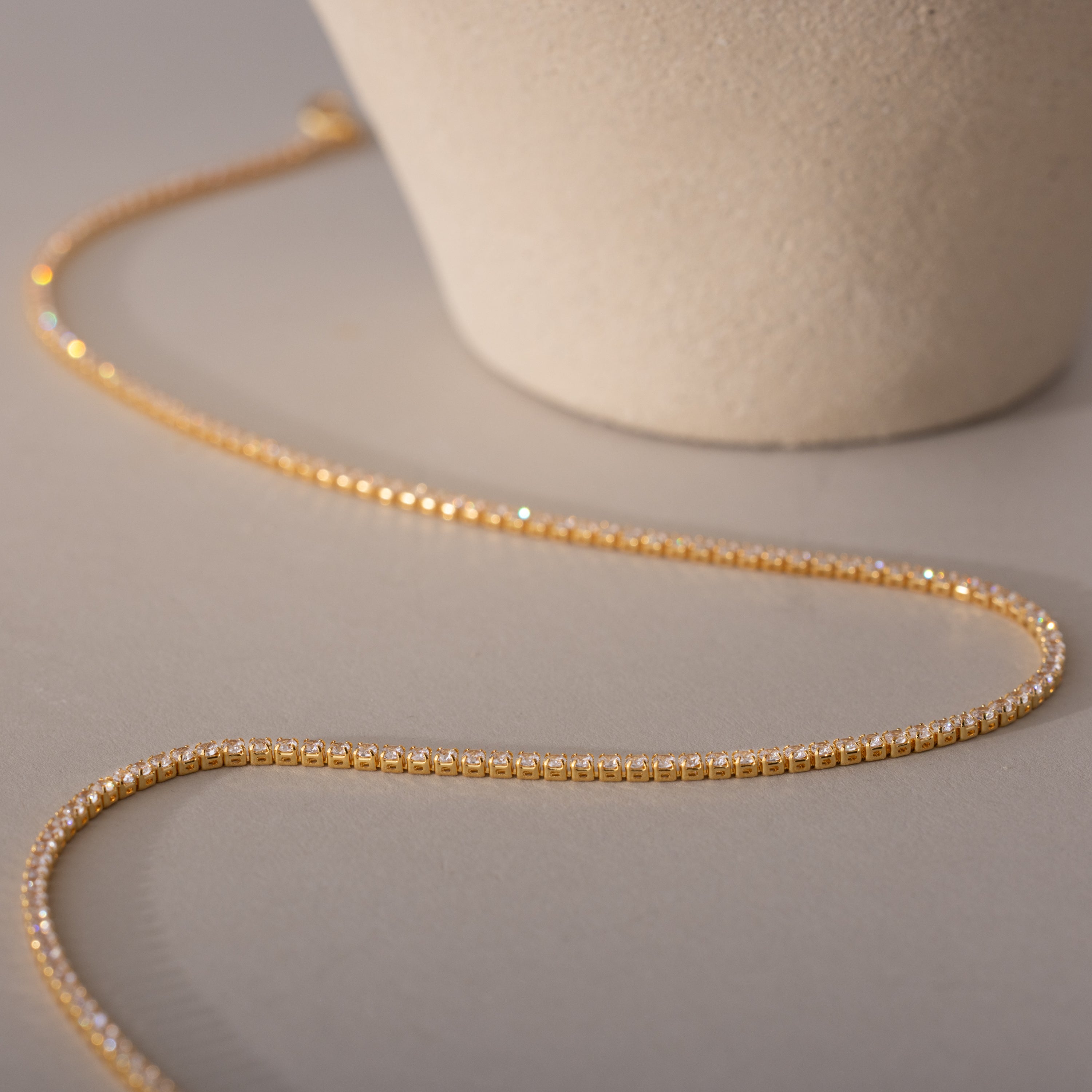 A detailed close-up of the Diamond Tennis Choker Necklace in 18K gold, laid flat on a neutral surface beside a ceramic object