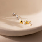 Two pairs of Heart Pearl Drop Earrings, in silver and gold with pearls, are displayed on a cream surface—perfect for any occasion.
