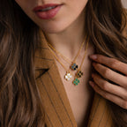Gemstone Clover Necklace trio with onyx, mother of pearl, and malachite stones on 18K gold chains worn layered on woman in.