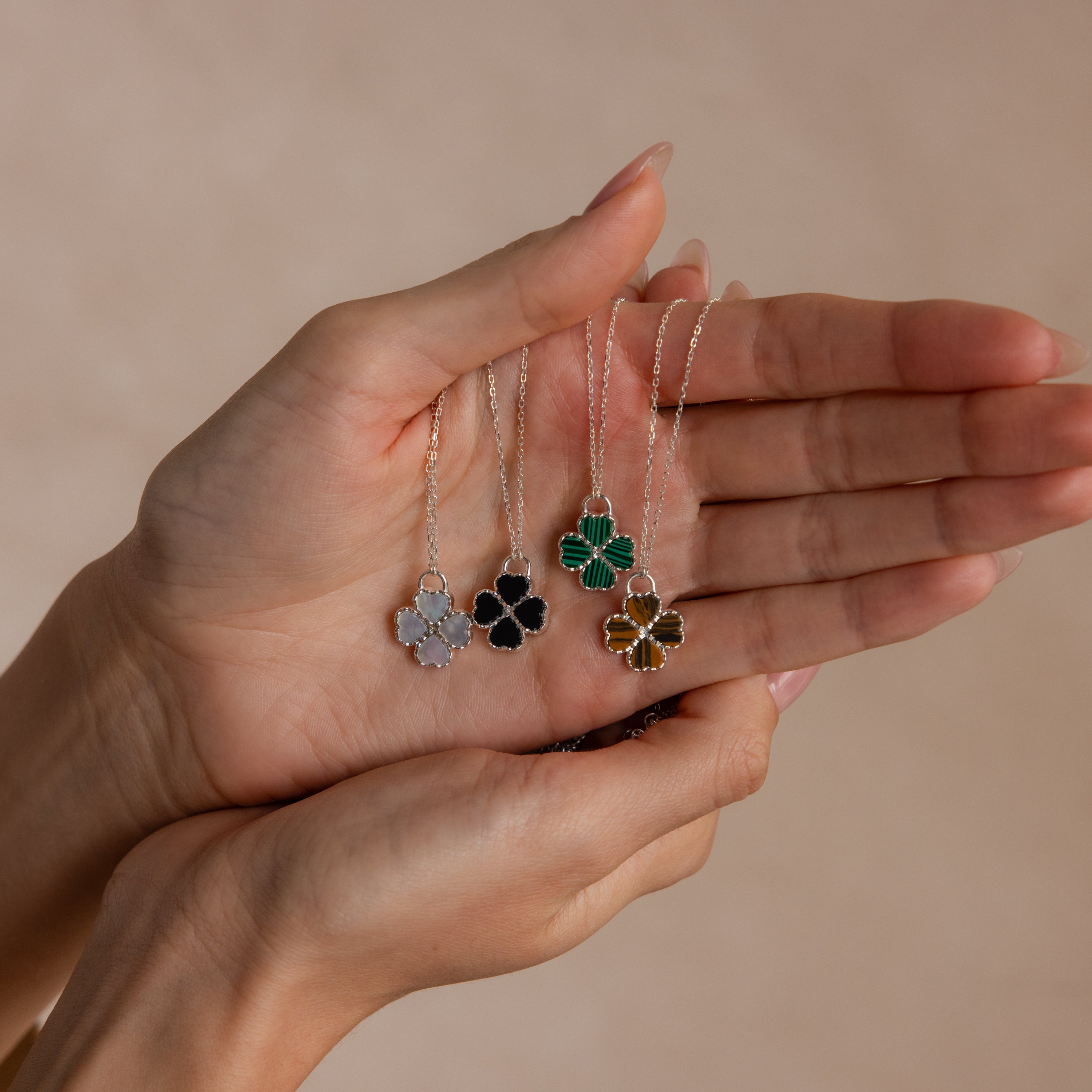 Gemstone Clover Necklace trio with onyx, malachite, and tiger’s eye gemstones on delicate chains held in hands against a.
