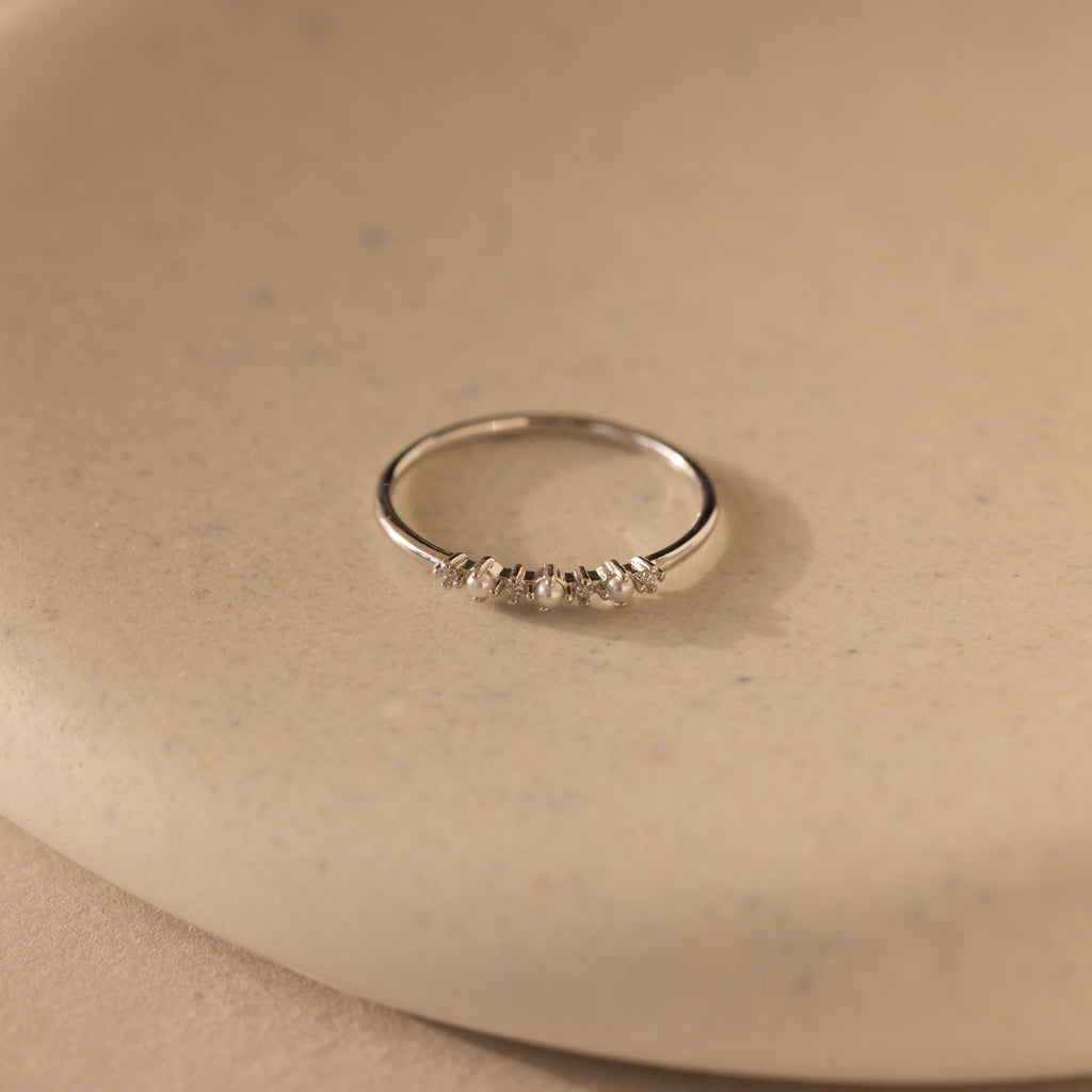 The Delicate Pearl Diamond Ring in Silver features small stones set on a smooth beige surface, perfect for stacking.