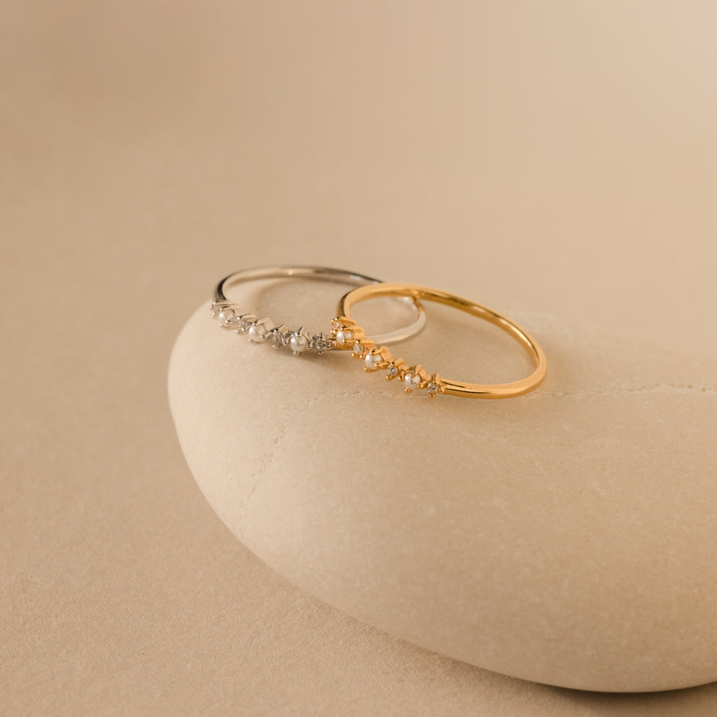The Delicate Pearl Diamond Ring rests on a smooth, beige stone against a neutral background.