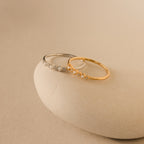 The Delicate Pearl Diamond Ring rests on a smooth, beige stone against a neutral background.