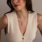 Model wearing a silver necklace with a heart hand charm, paired with a cream knit sleeveless top.