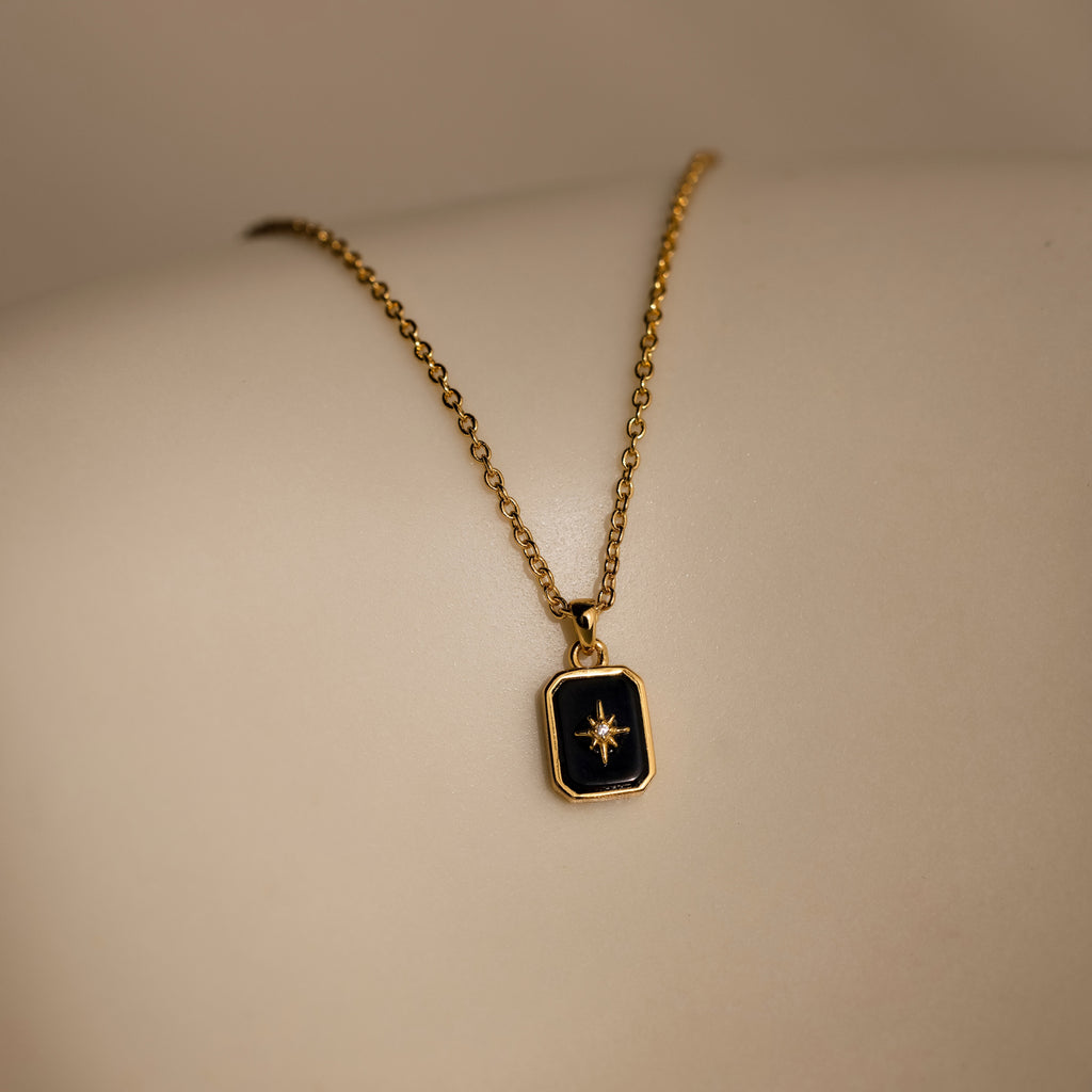 The North Star Gemstone Necklace in 18K Gold features a rectangular black onyx pendant with a star design, shown on a light skin tone.
