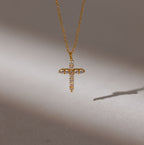 The Pave Cross Necklace in 18K Gold features a diamond-studded pendant casting a shadow on a neutral background—ideal for fans of elegant jewelry.