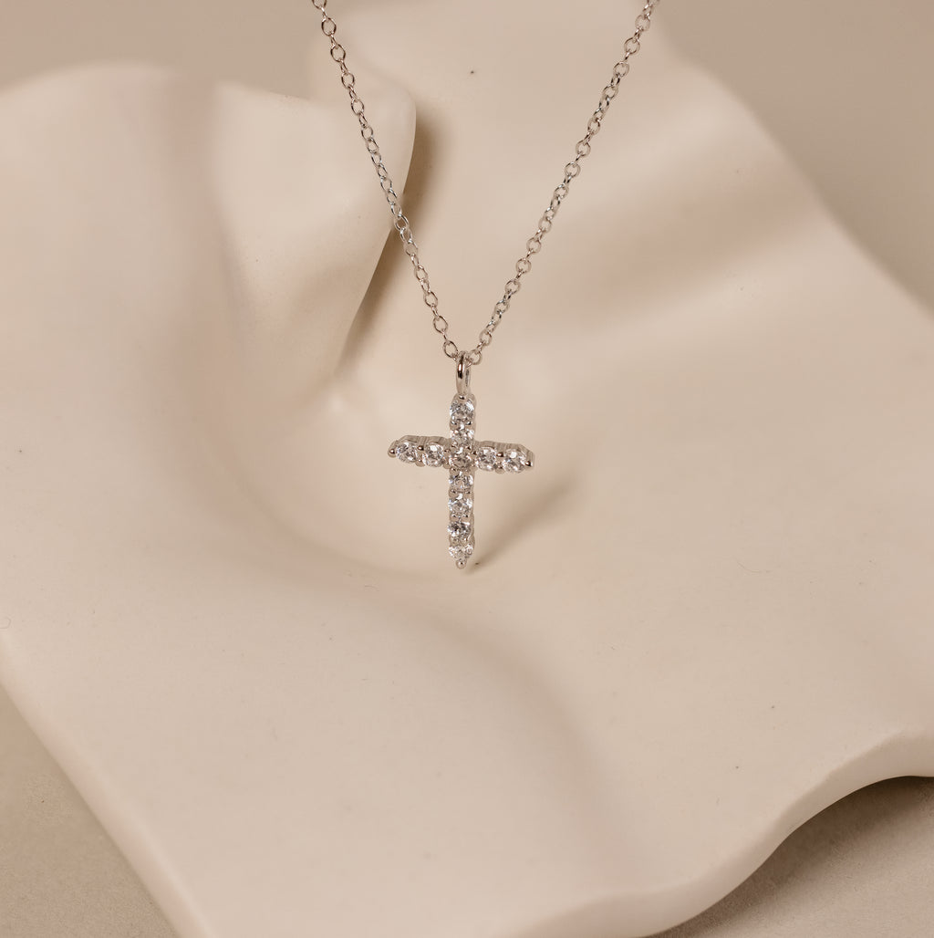 Discover elegance with the Pave Cross Necklace in Silver—a diamond-studded cross pendant on a sleek silver chain, beautifully showcased against a wavy cream-colored backdrop.
