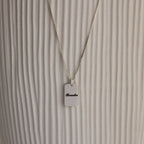 Name Tag Necklace in Sterling Silver with a rectangular pendant engraved "Brooke," shown on a textured white background.