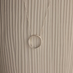 Inner Circle Necklace in Sterling Silver, featuring a simple circular pendant on a chain, shown against a textured beige background.