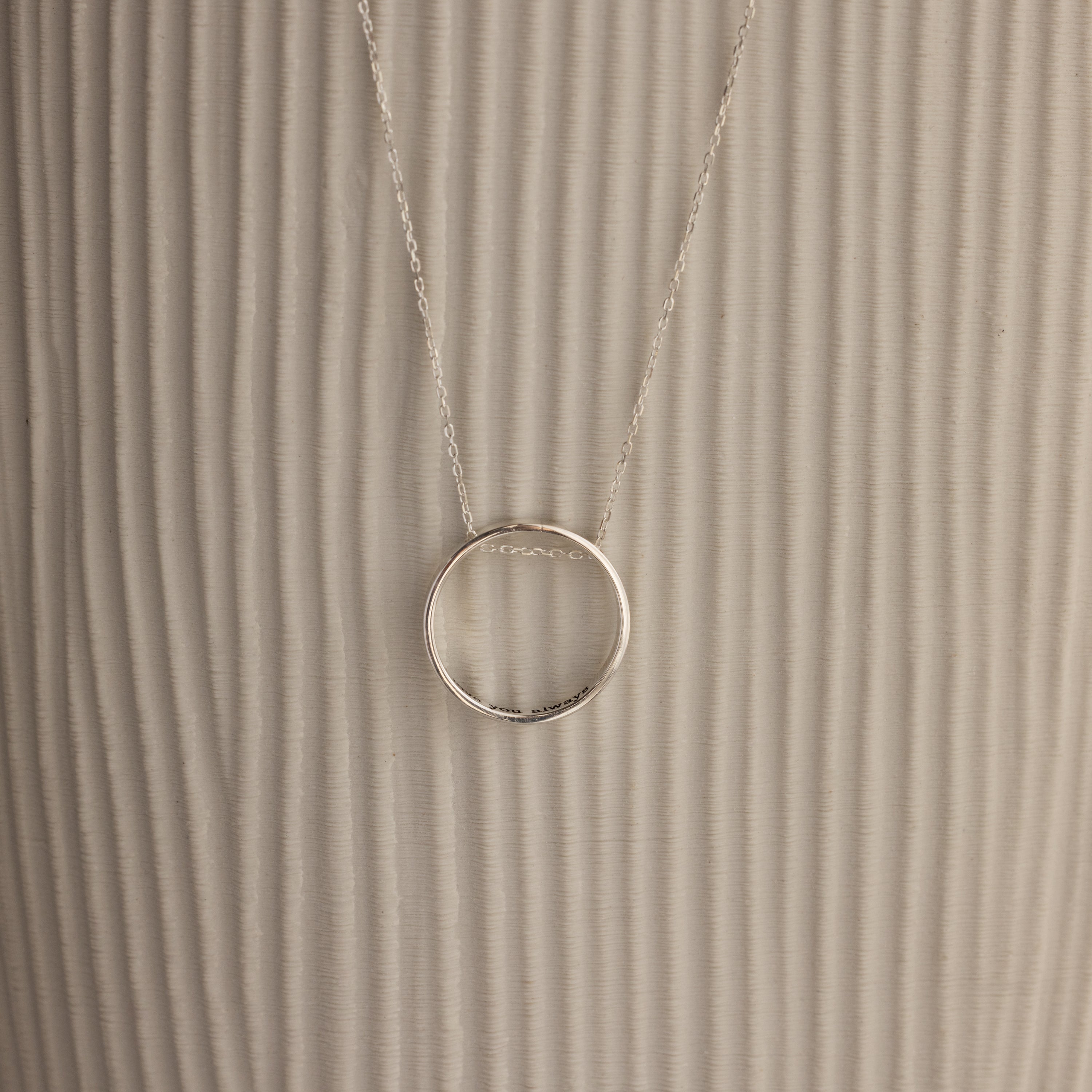 Inner Circle Necklace in Sterling Silver, featuring a simple circular pendant on a chain, shown against a textured beige background.