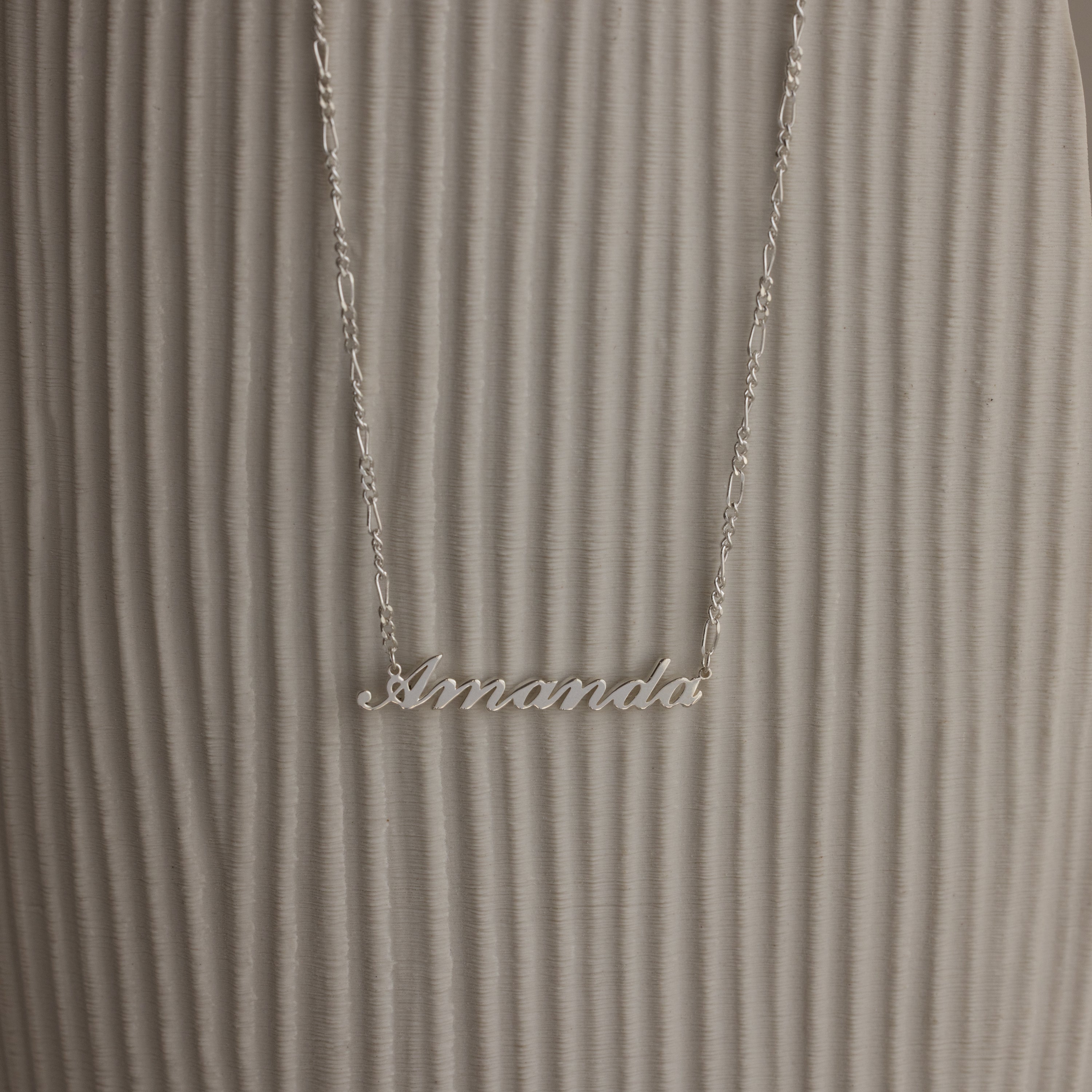 Silver necklace with 'Amanda' pendant on a textured white surface