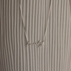 The Callie Box Chain Name Necklace features "Everly" in cursive on a delicate chain, shown against a textured, light background.