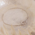 The Hinged Circle Charm Bracelet in Sterling Silver features two interlocking circles and is showcased on a soft, light-textured background for a delicate, minimal look.