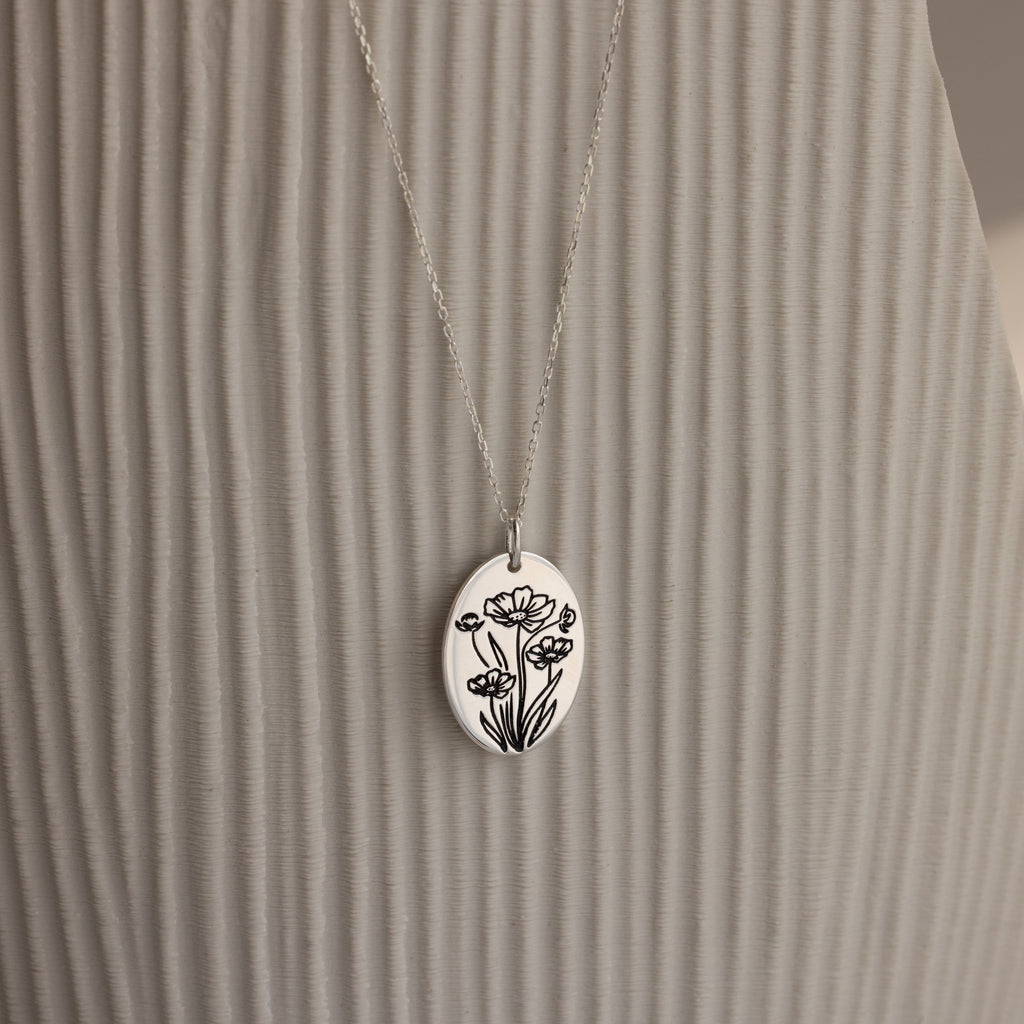The Oval Flower Necklace in Sterling Silver features a delicate floral engraving on an oval pendant, hanging from a fine chain—a timeless accessory for lovers of personalized jewelry.