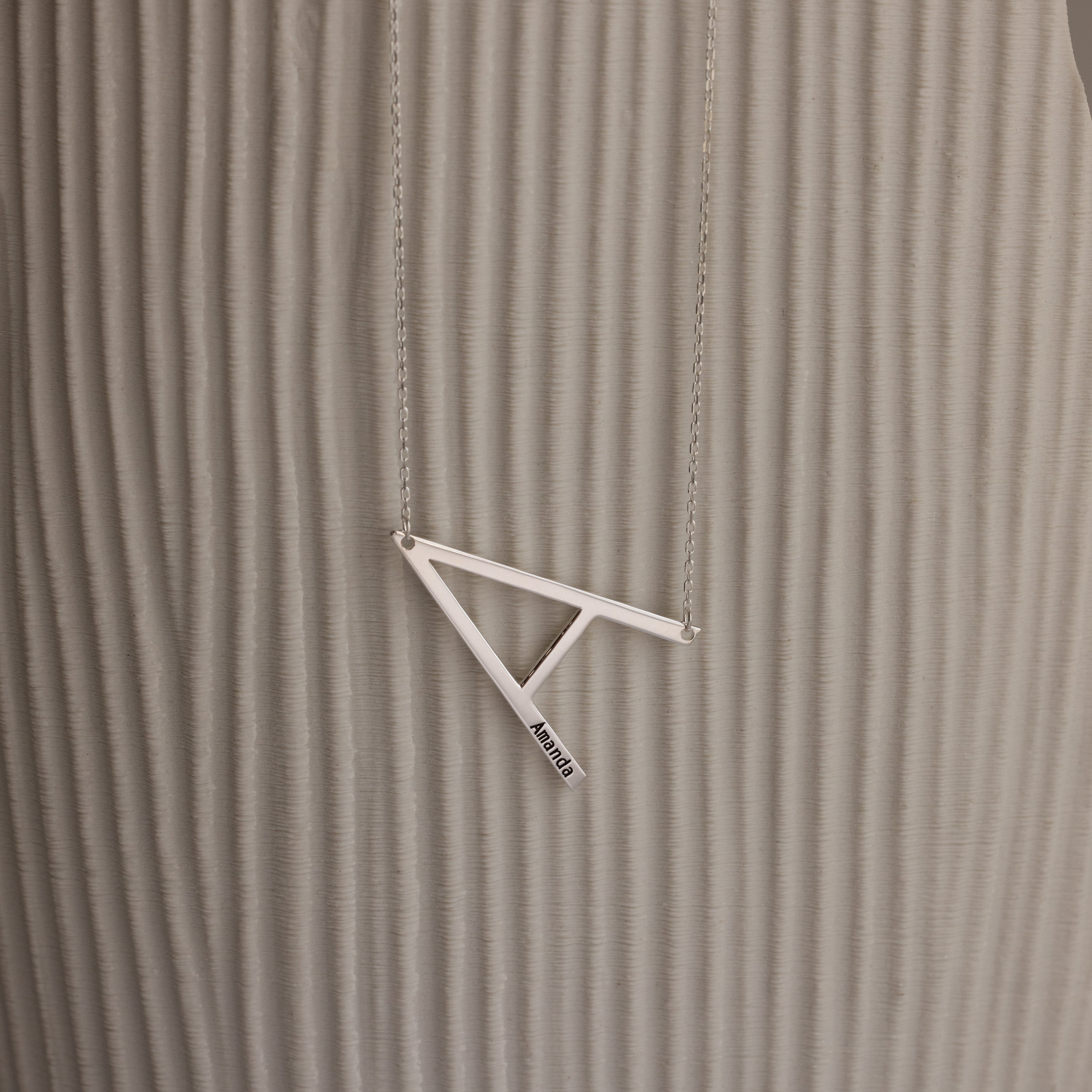 Large Sideways Initial Necklace in Sterling Silver showcased on a textured beige background.