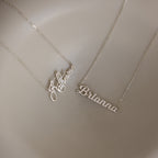 Two Mellow Name Necklaces in Sterling Silver rest on a beige surface, each featuring a unique script—one spelling Katherine and the other Brianna. Personalize your own Mellow Name Necklace for a custom look.