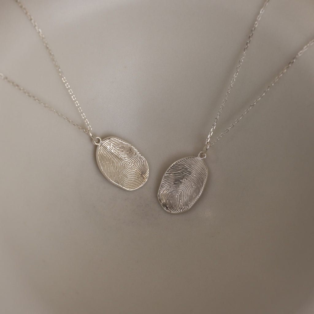 The Custom Fingerprint Necklace in Sterling Silver set features two oval pendants engraved with detailed fingerprints, making a stunning example of personalized jewelry displayed side by side.