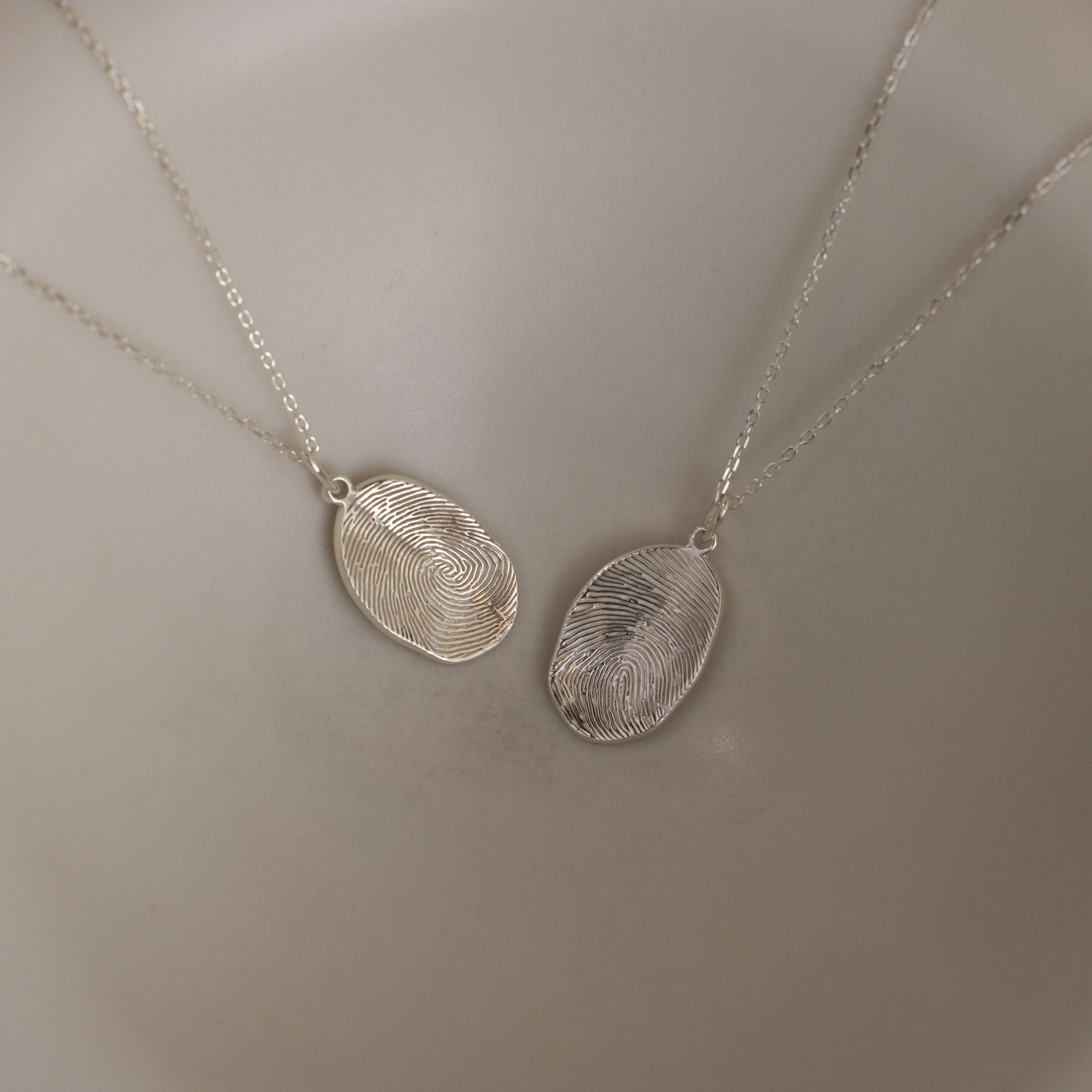The Custom Fingerprint Necklace in Sterling Silver set features two oval pendants engraved with detailed fingerprints, making a stunning example of personalized jewelry displayed side by side.
