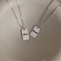 Two Name Tag Necklaces in Sterling Silver with rectangular pendants showcase personalized engraving—elegant jewelry featuring the names "Alexis" and "Brooke" on a sleek, plain surface.