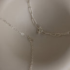 The Dainty Link Chain Necklace in Sterling Silver, ideal for necklace layering, is shown with different clasps and arranged on a neutral, light background.