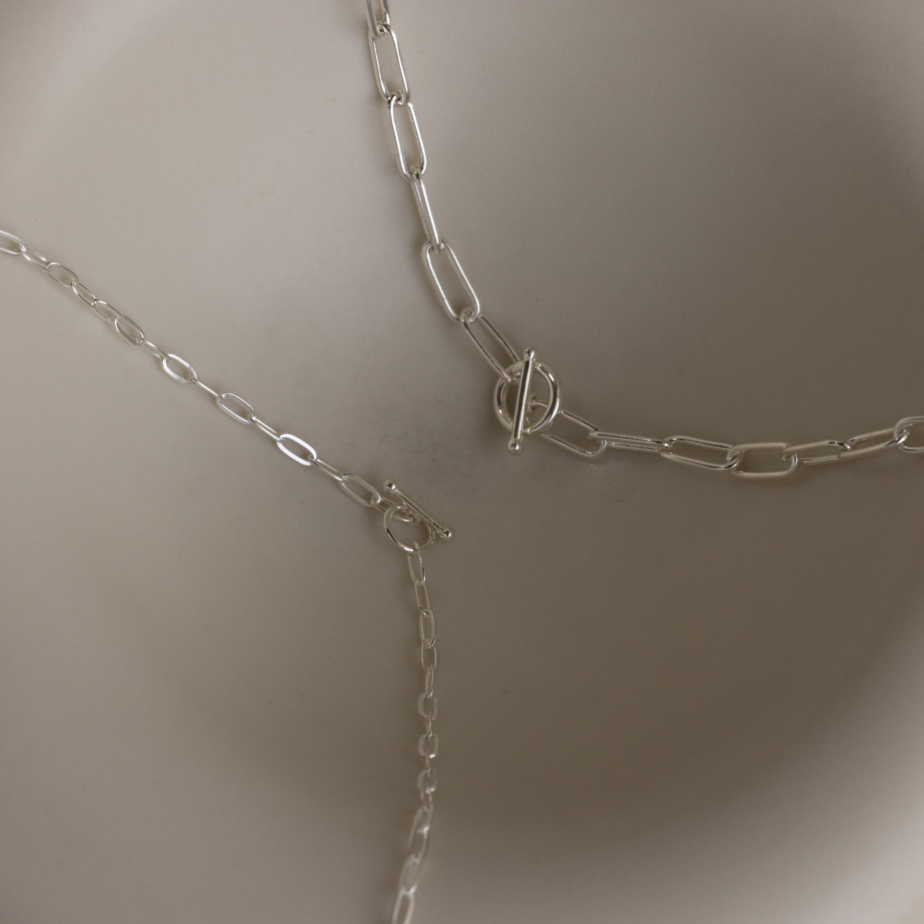 The Dainty Link Chain Necklace in Sterling Silver, ideal for necklace layering, is shown with different clasps and arranged on a neutral, light background.