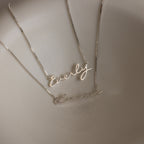 Two Callie Box Chain Name Necklaces in Sterling Silver, each with elegant cursive script on a delicate chain, are displayed on a smooth, cream-colored surface—ideal as customizable charms to suit any style.