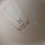 Two delicate sterling silver necklaces, including a Pave Initial Necklace with an "M" pendant and a personalized necklace spelling out "CECILIA," are displayed on a neutral background.